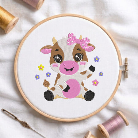 An embroidered design of a cute sitting baby cow with brown patches, big shiny eyes, a pink floral bow, and colorful flowers, stitched inside a wooden hoop on white fabric with sewing threads.
