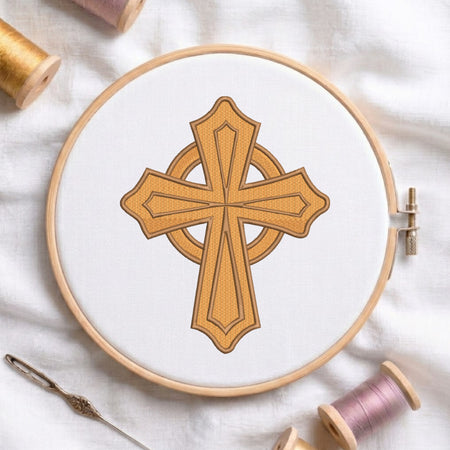 A circular embroidery hoop holding white fabric with a stitched golden cross design, surrounded by spools of thread and a needle on a white fabric background.