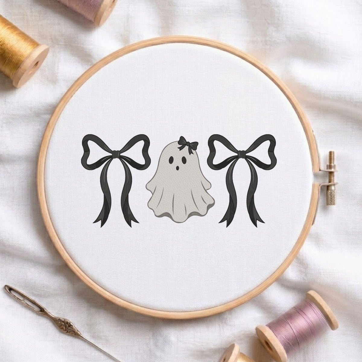 Cute ghost wearing a hair bow flanked by large black bows machine embroidery design shown in a wooden embroidery hoop on white fabric with thread spools and a needle   