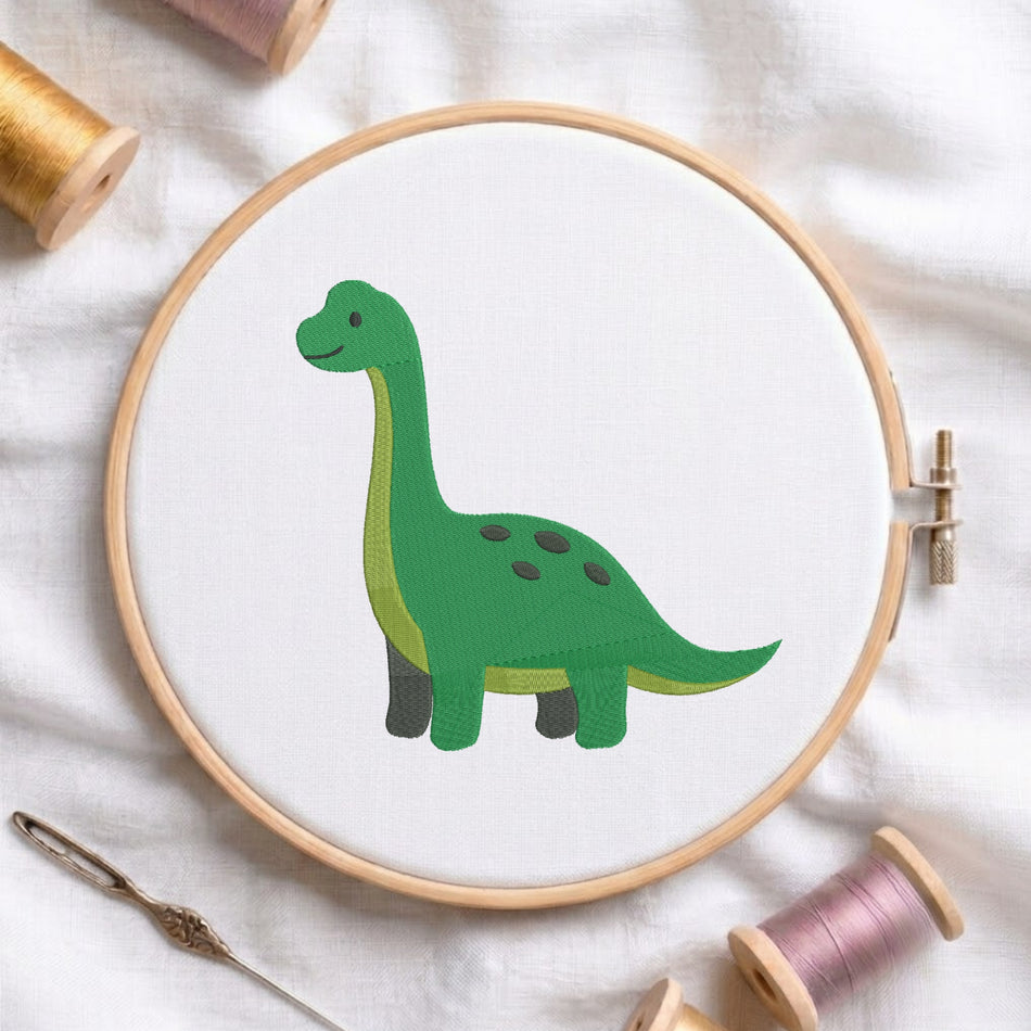 A wooden embroidery hoop holding white fabric with a green long-neck dinosaur design, surrounded by embroidery thread spools and a needle on a white cloth background.
