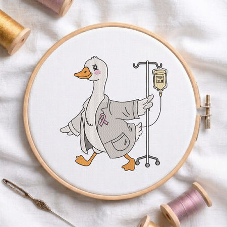 An embroidered design of a cute white duck wearing a doctor's lab coat and a pink awareness ribbon, walking with an IV pole, stitched inside a wooden hoop on white fabric with sewing threads.