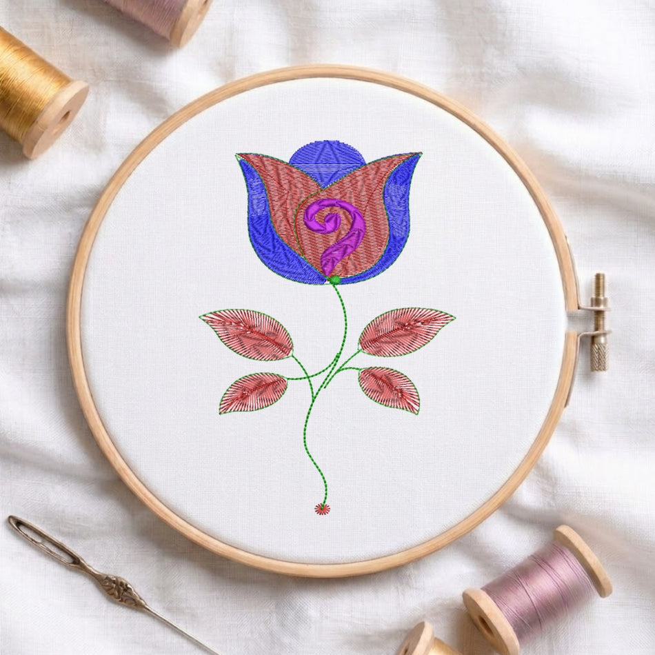 A circular embroidery hoop holding white fabric with a stylized floral design in blue, pink, purple, and green thread, surrounded by spools of thread and a needle on a white fabric background.