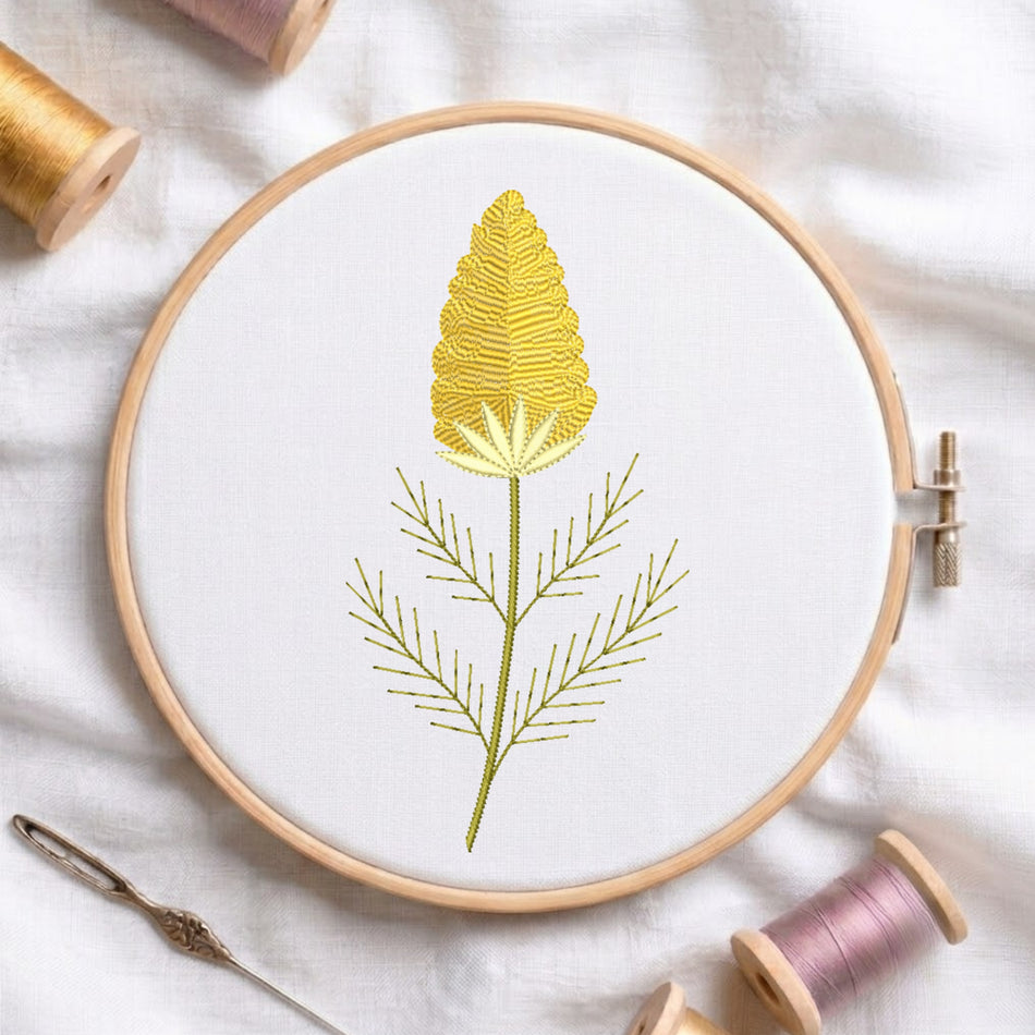 A circular embroidery hoop holding white fabric with a yellow and olive green embroidered flower design, surrounded by spools of thread and a needle on a white fabric background.