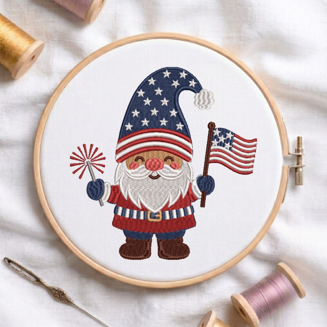 Embroidery hoop with a gnome design holding an American flag and firework, surrounded by embroidery threads on a light background.