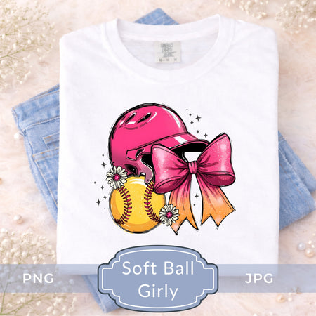 A folded white T-shirt displayed on top of light blue jeans, featuring a colorful graphic of a pink softball helmet, yellow softball, and pink bow with daisies. Text overlay at the bottom reads 'Soft Ball Girly' with PNG and JPG labels.