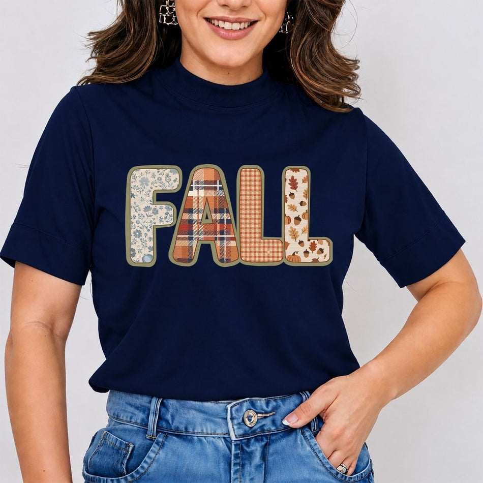 A woman wearing a navy blue short-sleeve t-shirt with a large 'FALL' graphic across the chest in autumn-themed patterned fabrics, paired with blue jeans.