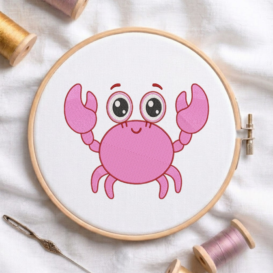 A round embroidery hoop holding white fabric with a pink cartoon crab design, surrounded by spools of thread and a needle on a white fabric background.