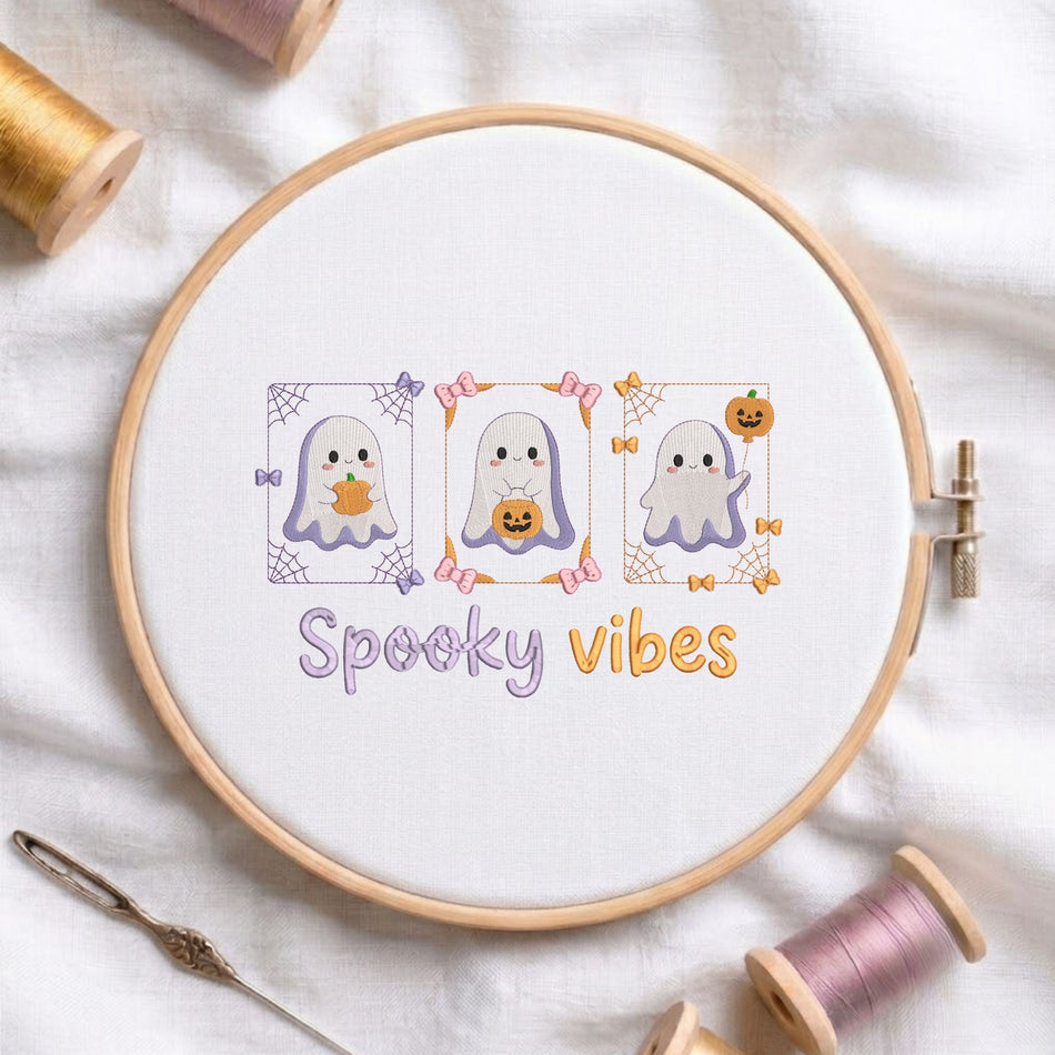 Cute spooky vibes ghost with pumpkins machine embroidery design displayed in a wooden hoop on white fabric with thread spools and a needle