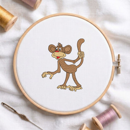 Cute funny monkey machine embroidery design displayed in a wooden hoop on white fabric with thread spools and a needle