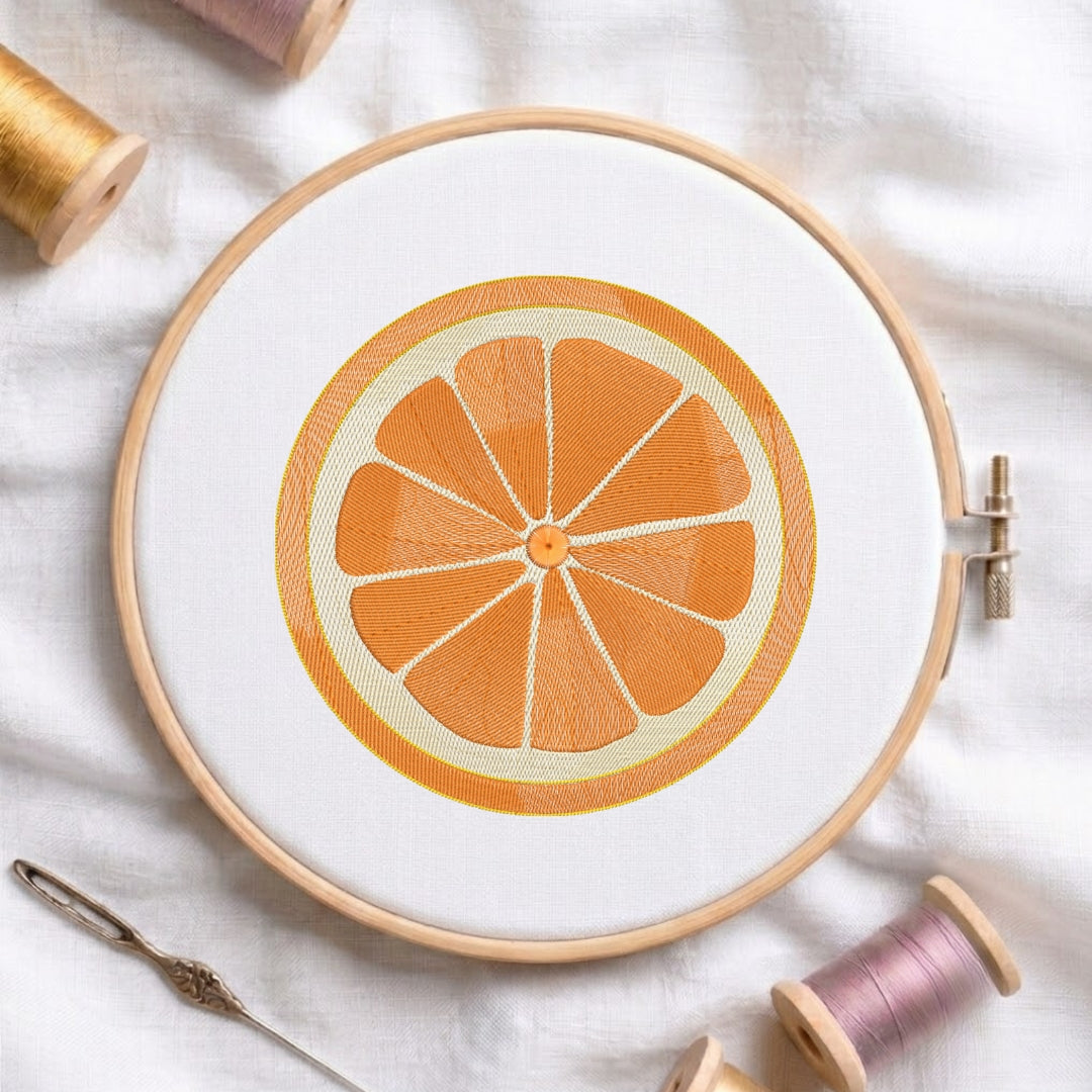 A circular embroidery hoop holding white fabric with an orange slice design stitched in orange and cream thread, styled on a white fabric background with spools of thread and a needle nearby.