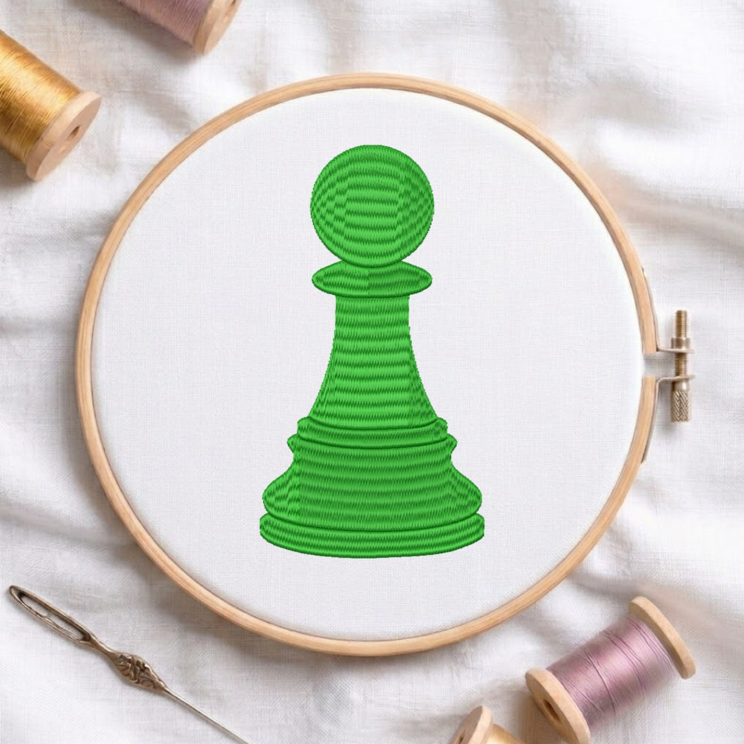 The green chess pawn design is secured in a wooden embroidery hoop, displayed with embroidery thread spools and a needle on a white fabric background.