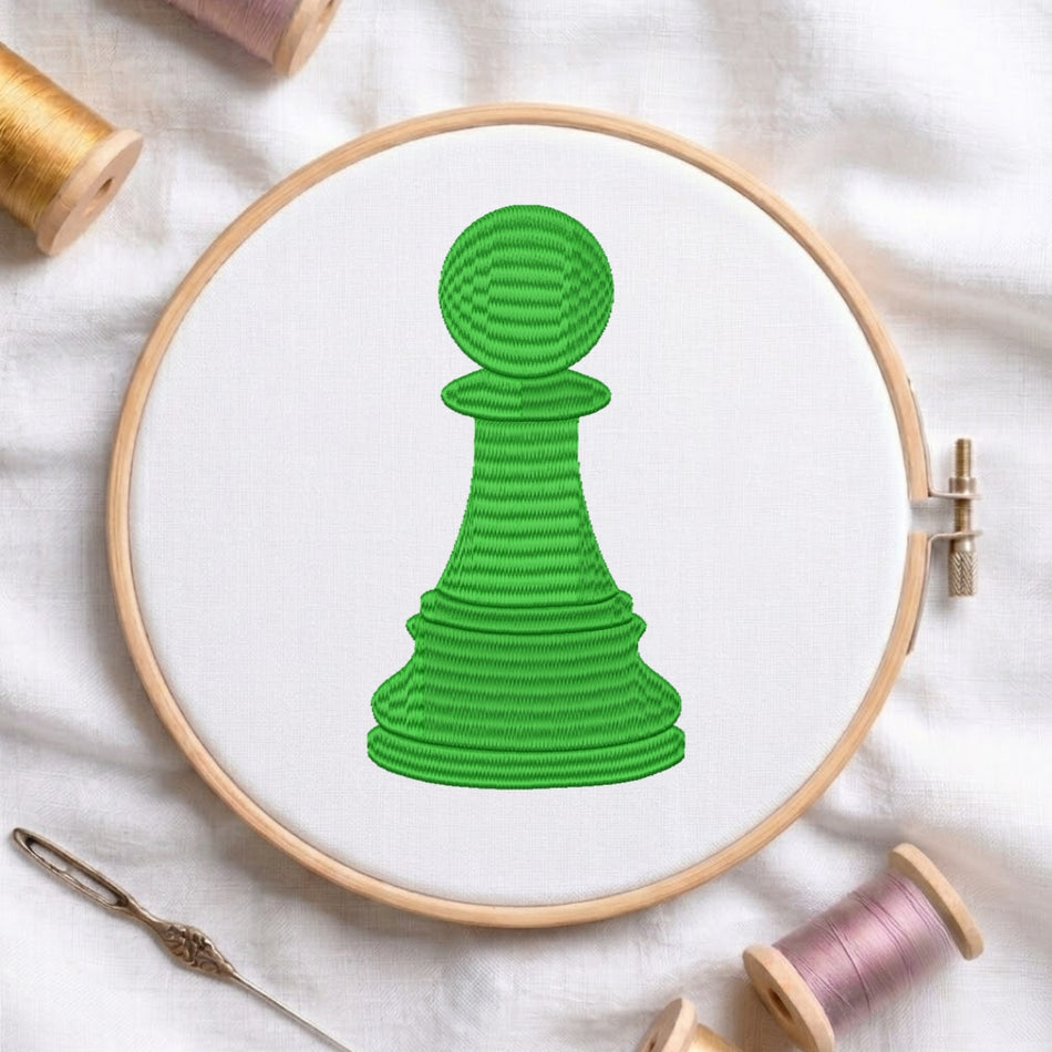 The green chess pawn design is secured in a wooden embroidery hoop, displayed with embroidery thread spools and a needle on a white fabric background.