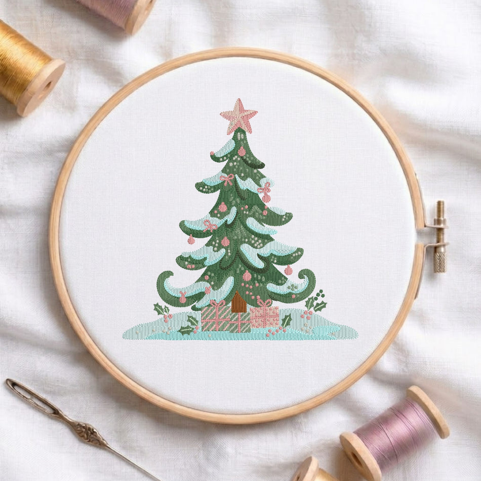 A circular embroidery hoop on white fabric, featuring a stitched Christmas tree with pink ornaments and gifts, surrounded by spools of thread and a needle as styled props.