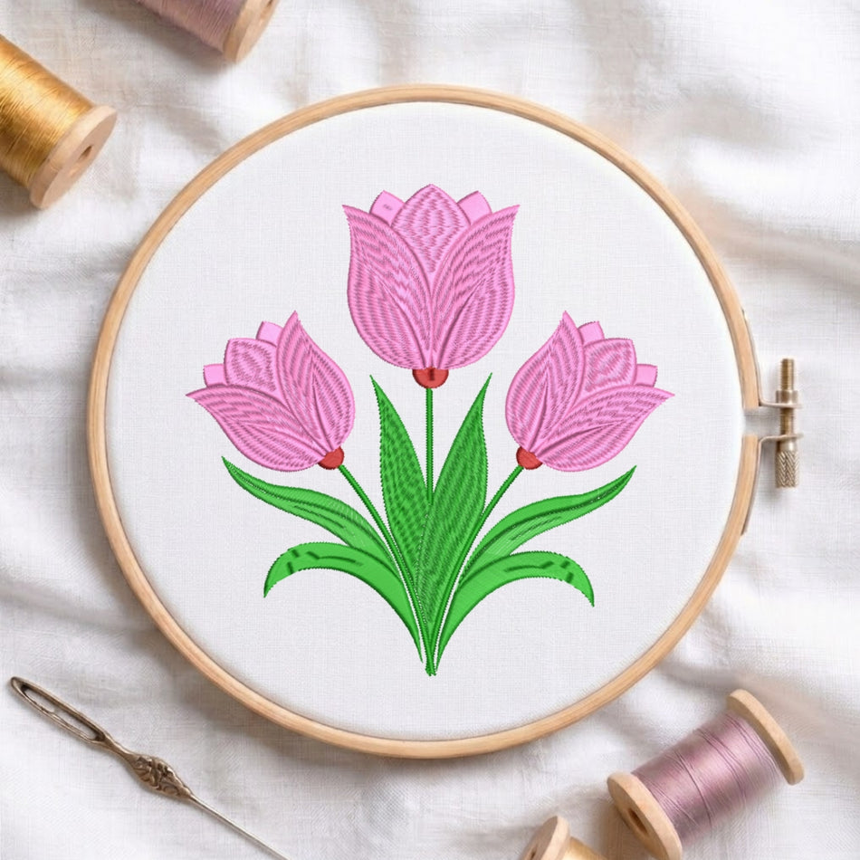 A circular embroidery hoop holding white fabric with a stitched tulip design in pink and green, surrounded by spools of thread and a needle on a white fabric background.