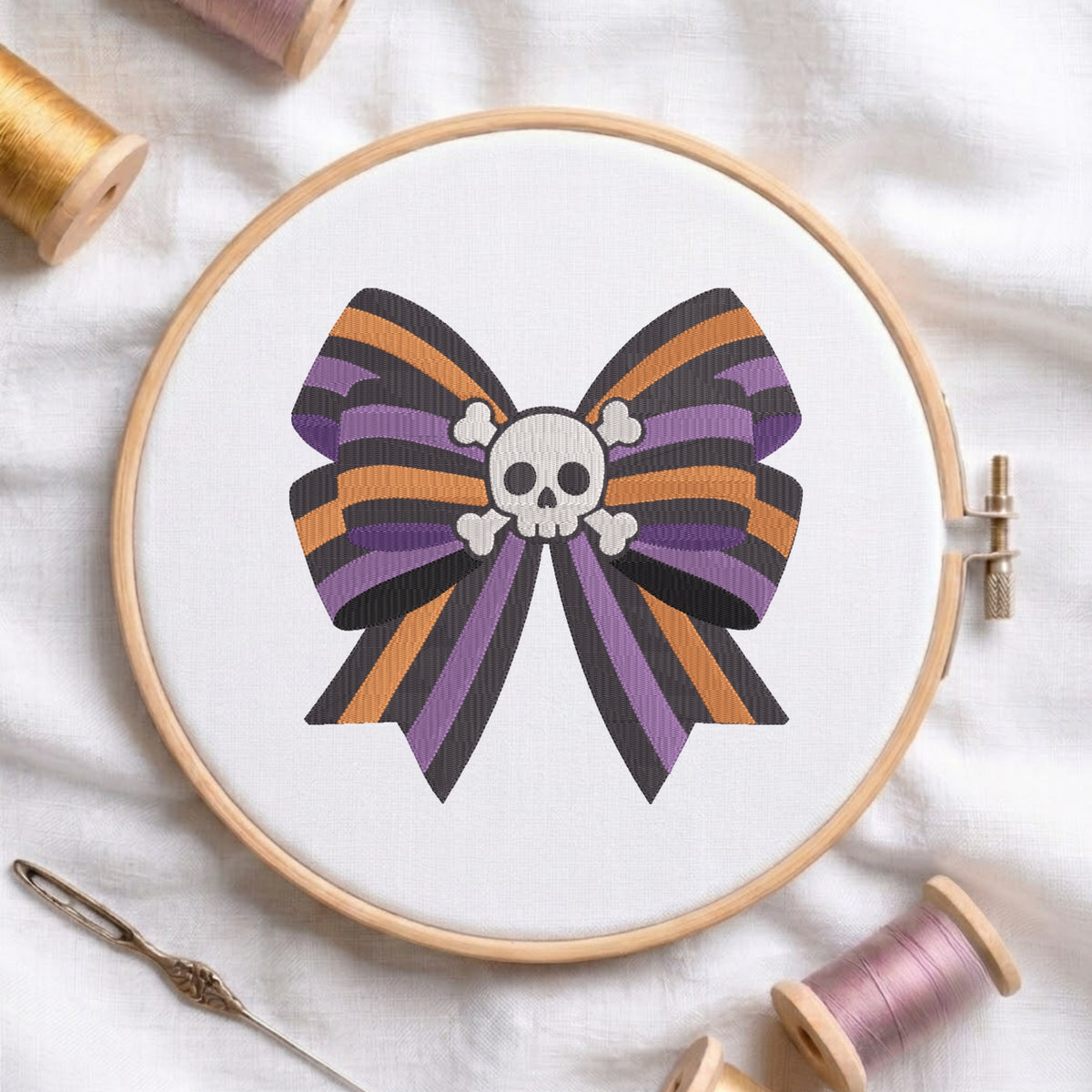 A white fabric stretched in a wooden embroidery hoop, featuring an embroidered design of a striped purple, orange, and black bow centered with a white skull and crossbones.