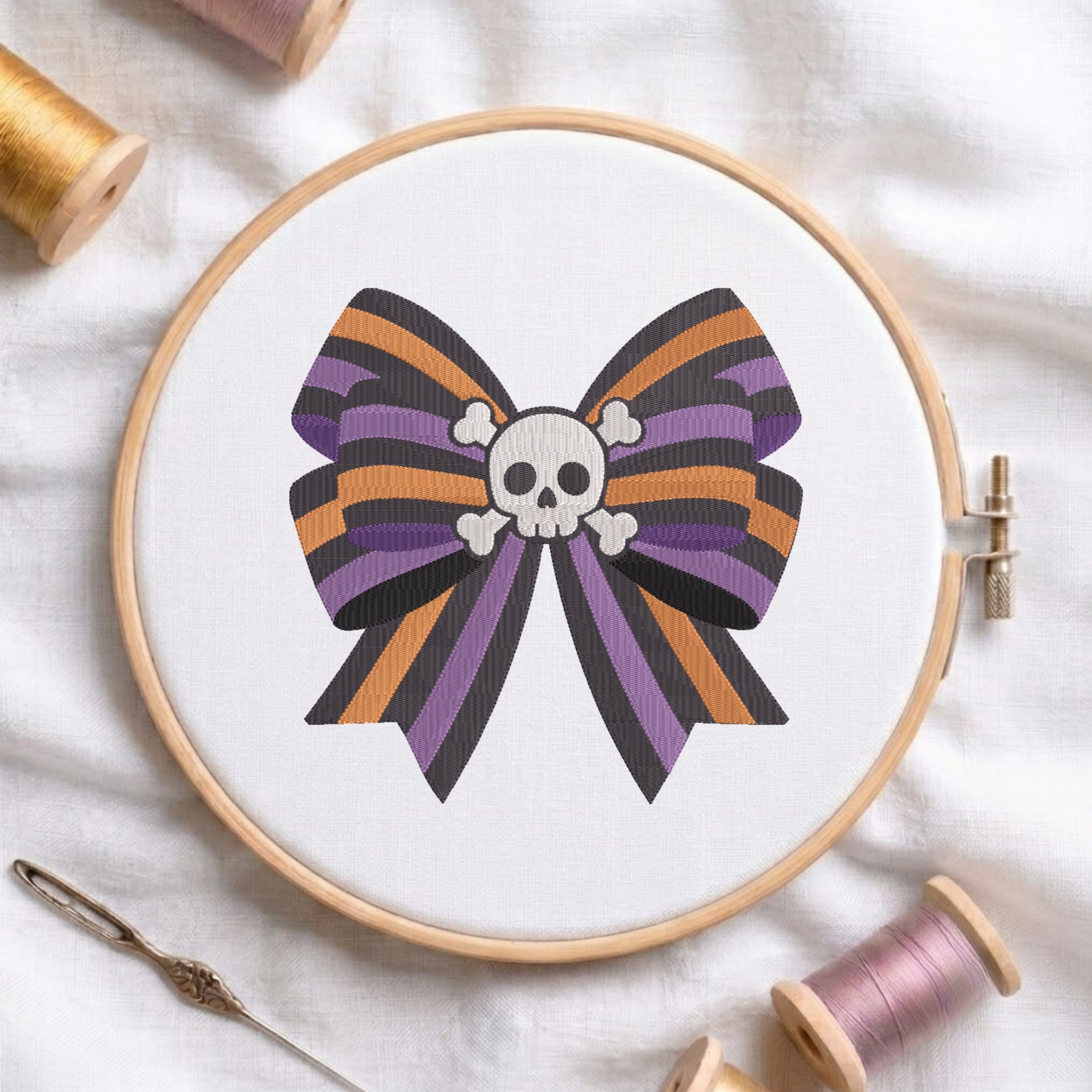 A white fabric stretched in a wooden embroidery hoop, featuring an embroidered design of a striped purple, orange, and black bow centered with a white skull and crossbones.