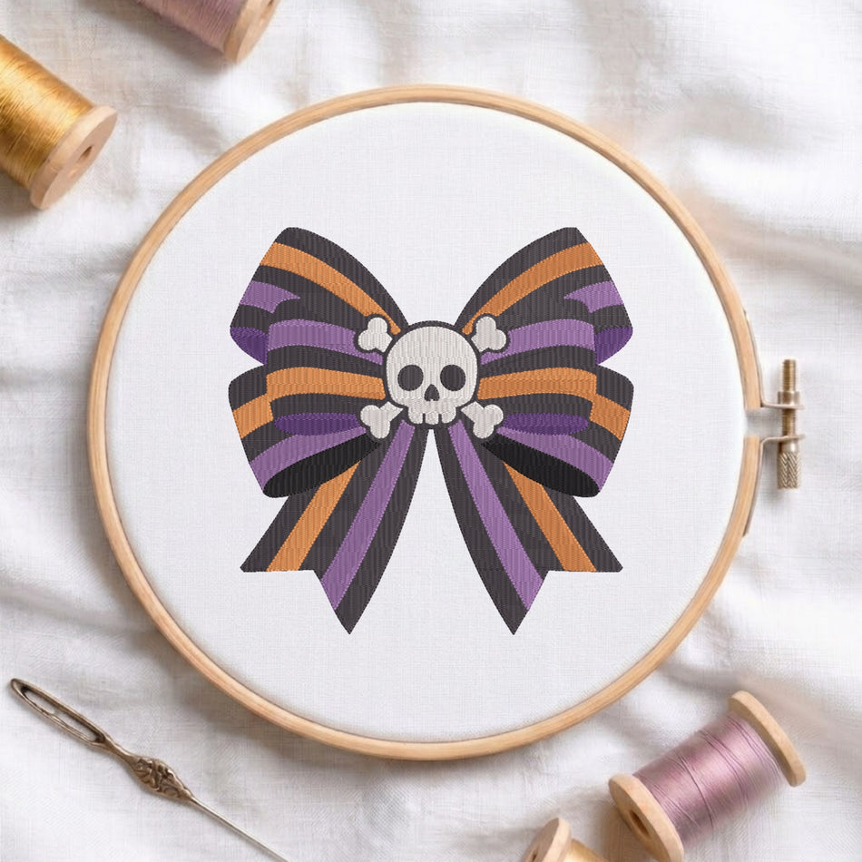 A white fabric stretched in a wooden embroidery hoop, featuring an embroidered design of a striped purple, orange, and black bow centered with a white skull and crossbones.