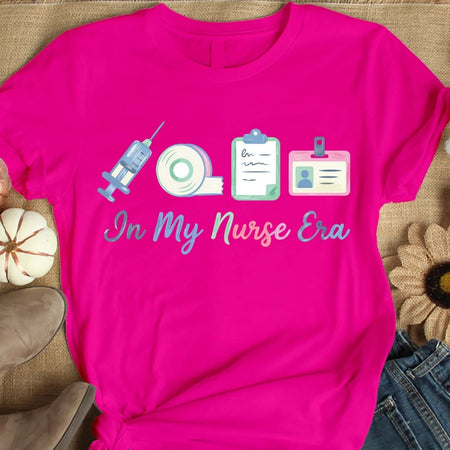 Pink t-shirt with nurse-themed graphics and text on a textured surface