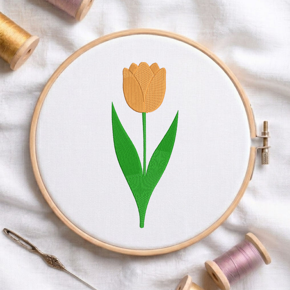 Bright yellow tulip blossom with green stem and leaves embroidered inside a round wooden hoop with thread spools.