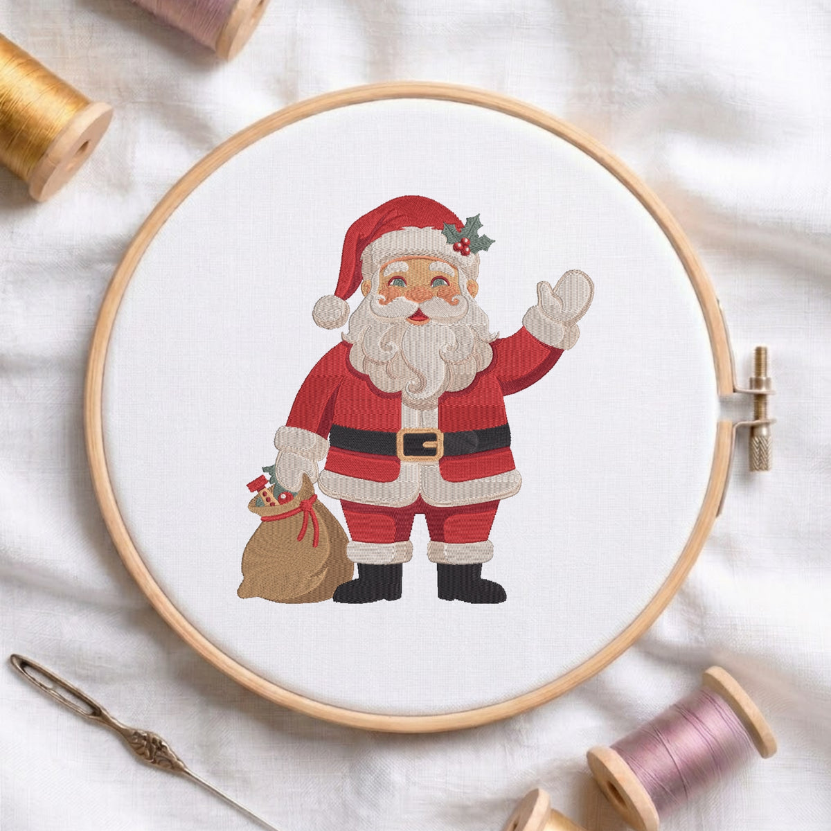 A circular embroidery hoop holds white fabric with a stitched illustration of Santa Claus waving and holding a sack, surrounded by spools of thread and a needle on a white fabric background.