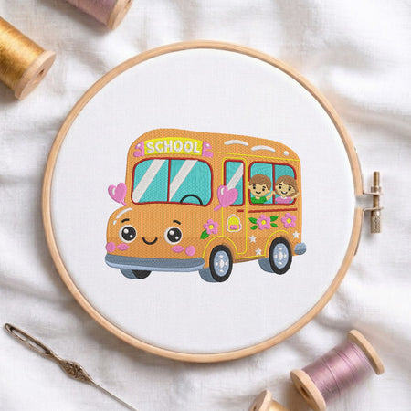 An embroidered design of a cheerful yellow school bus with cute eyes, pink hearts, and kids waving from the window, stitched inside a wooden hoop on white fabric with sewing threads.