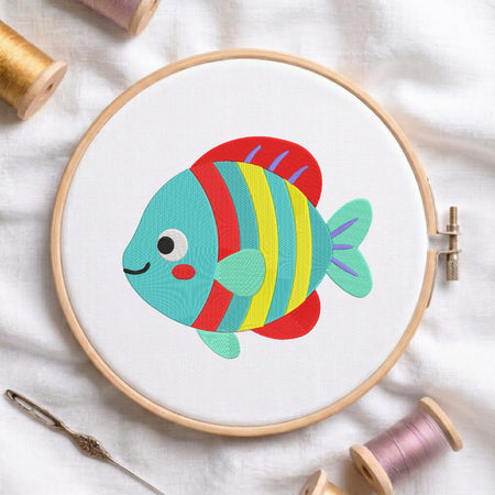 Cute colorful striped tropical fish embroidery design centered inside a wooden embroidery hoop on white fabric with spools of thread.