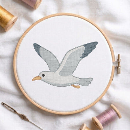Flying seagull bird machine embroidery design framed inside a round wooden hoop with thread spools.
