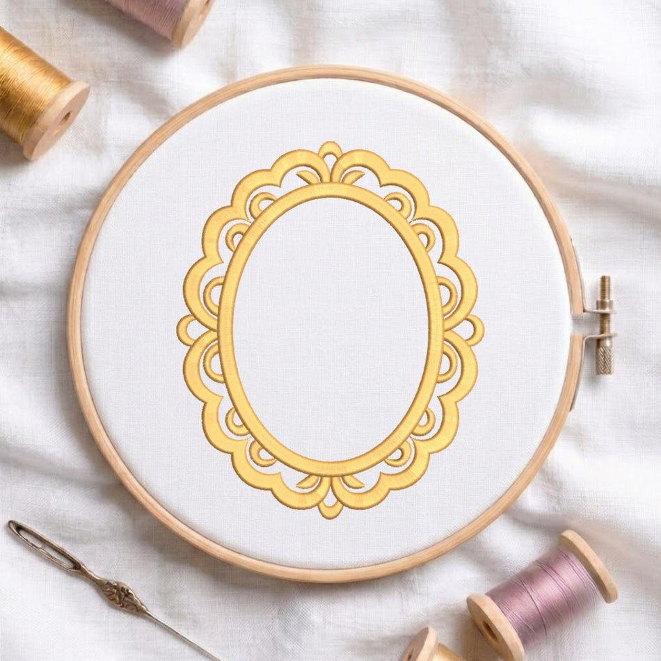 A circular embroidery hoop holding white fabric with a decorative gold ornamental frame design, styled on a white cloth with thread spools and a needle around it.