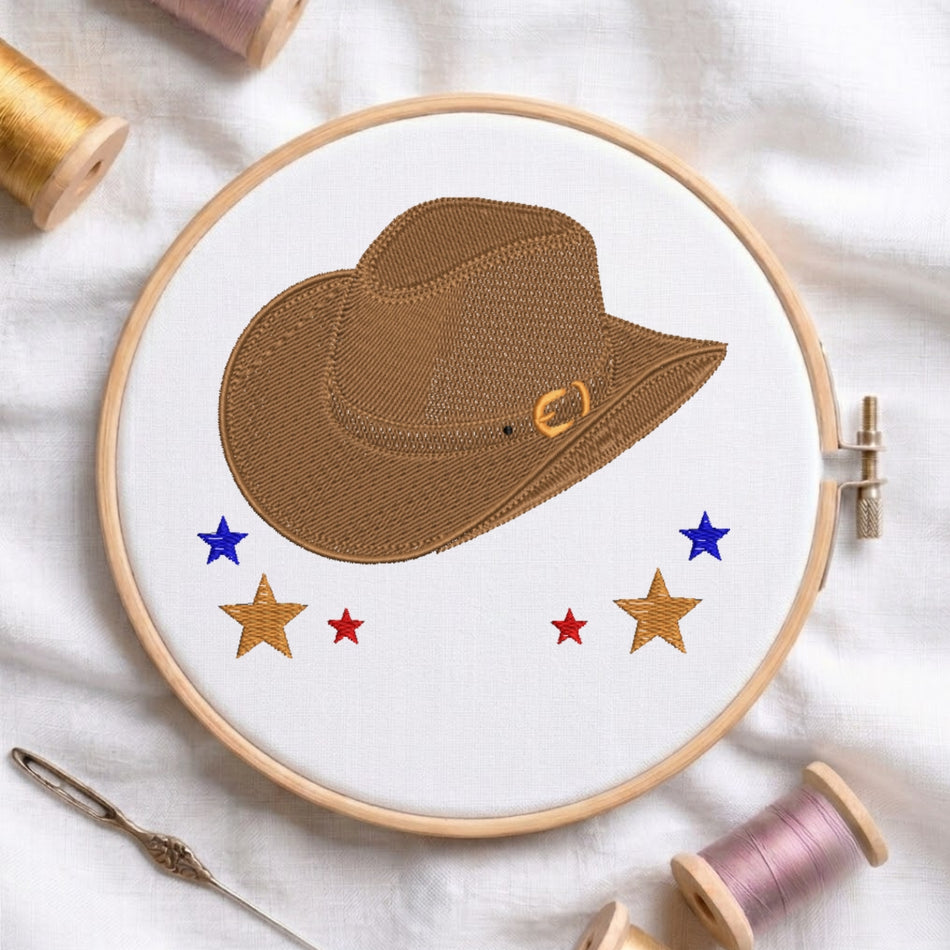 Embroidery hoop with a brown cowboy hat and stars on a white fabric background.
