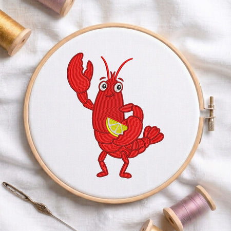 A circular embroidery hoop holding white fabric with a red cartoon lobster holding a yellow lemon slice. The hoop is styled on a white fabric background with spools of thread and a needle.