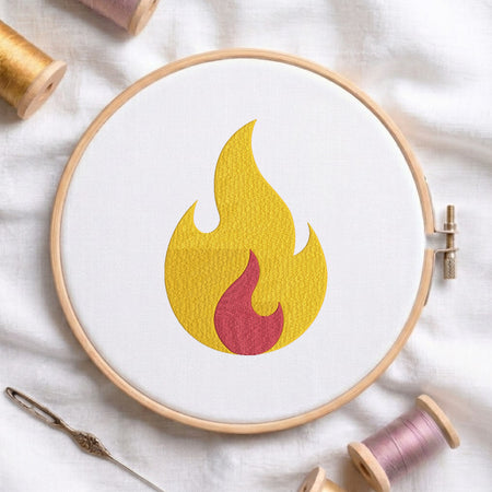 A circular embroidery hoop holding white fabric with a stylized flame motif in yellow and red, surrounded by spools of thread and a needle on a white fabric background.