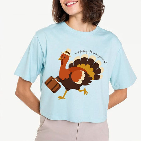 A woman wearing a light blue cropped t-shirt with a cartoon turkey graphic carrying a suitcase and the text 'not today, Thanksgiving!'.