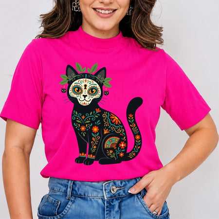 A smiling woman wearing a hot pink high-neck t-shirt printed with a highly detailed black cat decorated in colorful Dia de los Muertos sugar skull patterns.