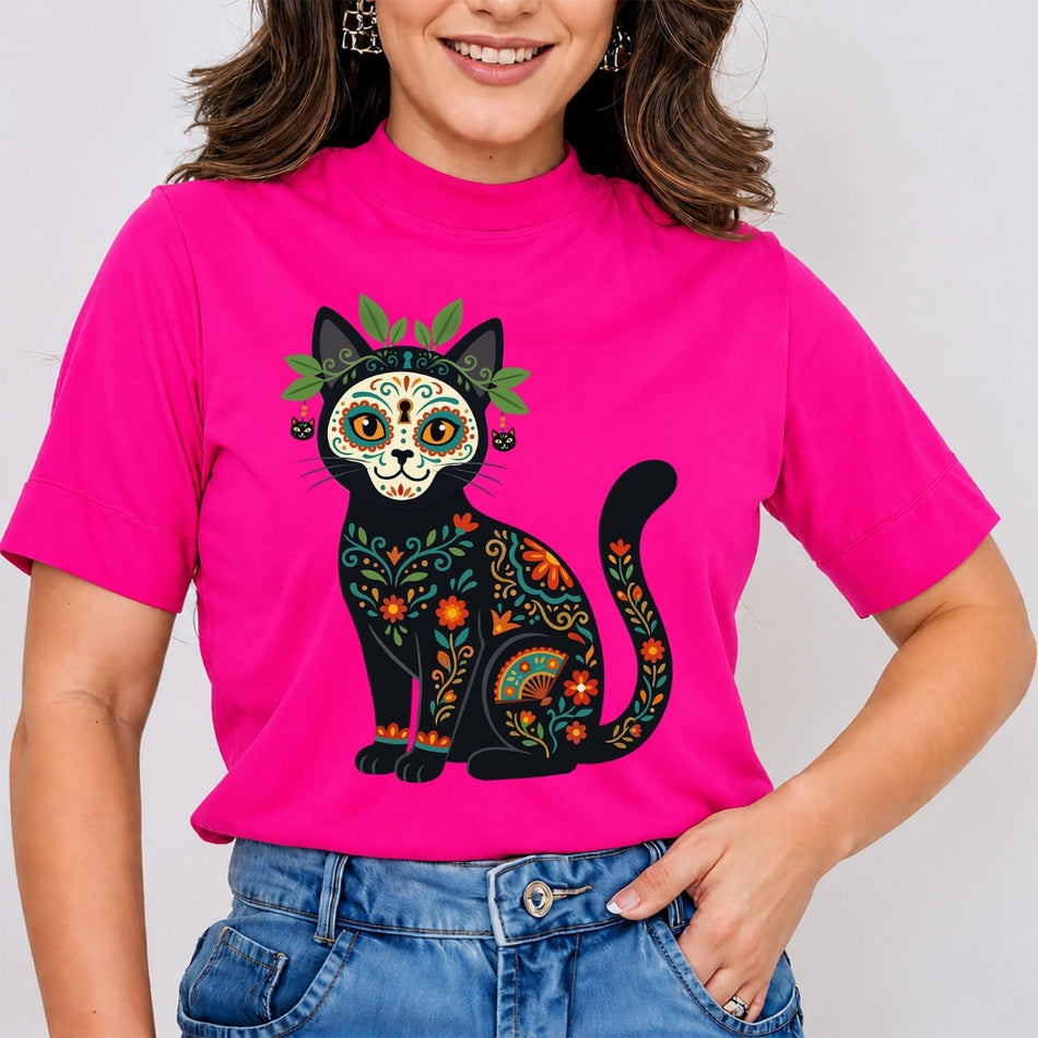 A smiling woman wearing a hot pink high-neck t-shirt printed with a highly detailed black cat decorated in colorful Dia de los Muertos sugar skull patterns.