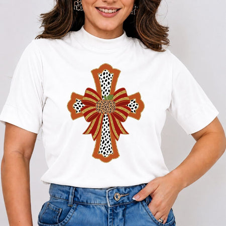 A woman wearing a white short-sleeve t-shirt with a large decorative cross graphic on the front. The graphic features red and brown ribbon-like stripes, black-and-white spotted sections, and a small green leaf detail at the center.