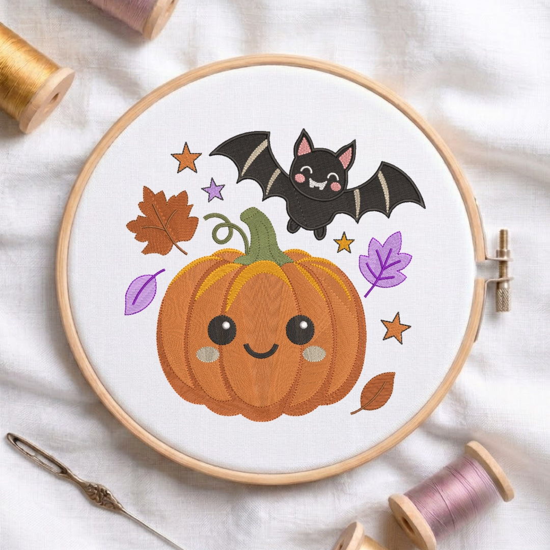 A circular embroidery hoop on white fabric, featuring a cute autumn design with a smiling orange pumpkin, a black bat, purple leaves, and gold stars. Spools of thread and a needle are arranged around the hoop.