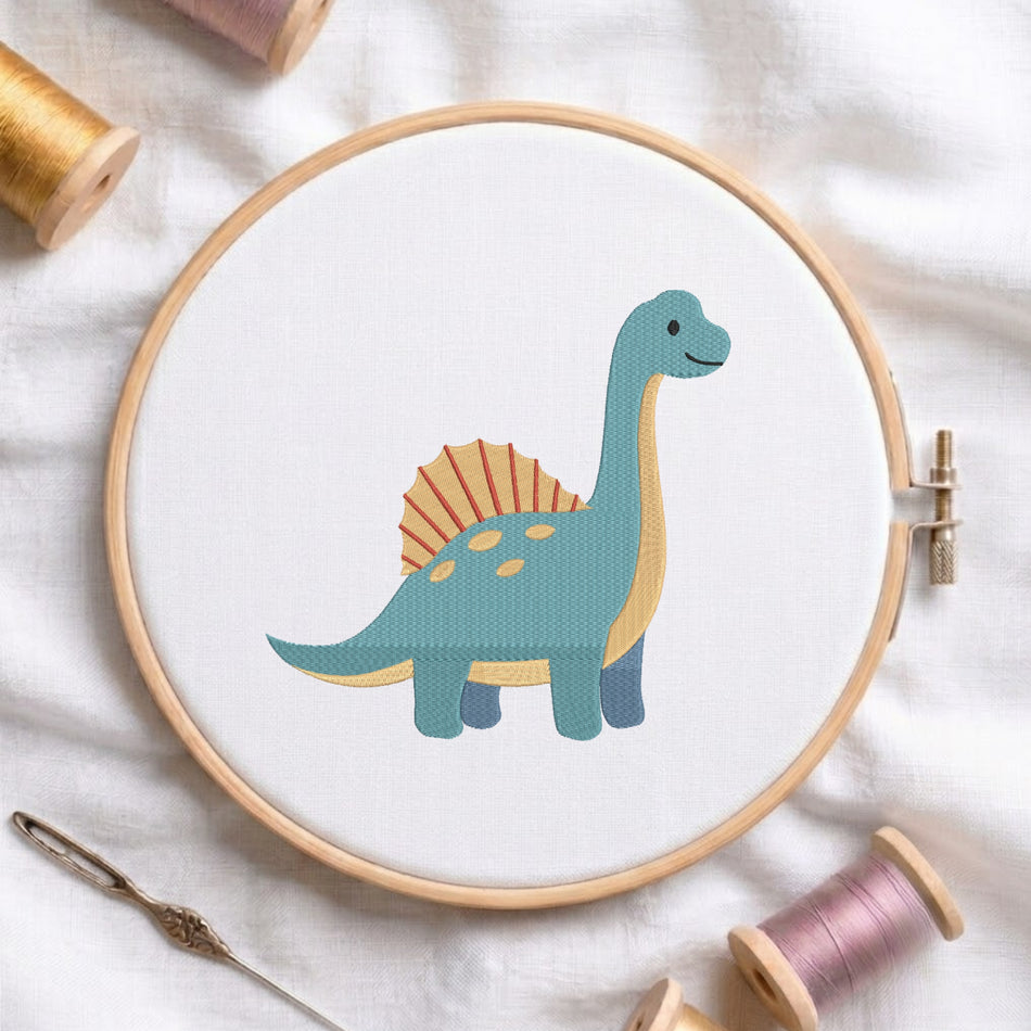 A circular embroidery hoop holding white fabric with a stitched cartoon brachiosaurus in teal, cream, and orange. The hoop is styled on a white fabric background with spools of thread and a needle around it.