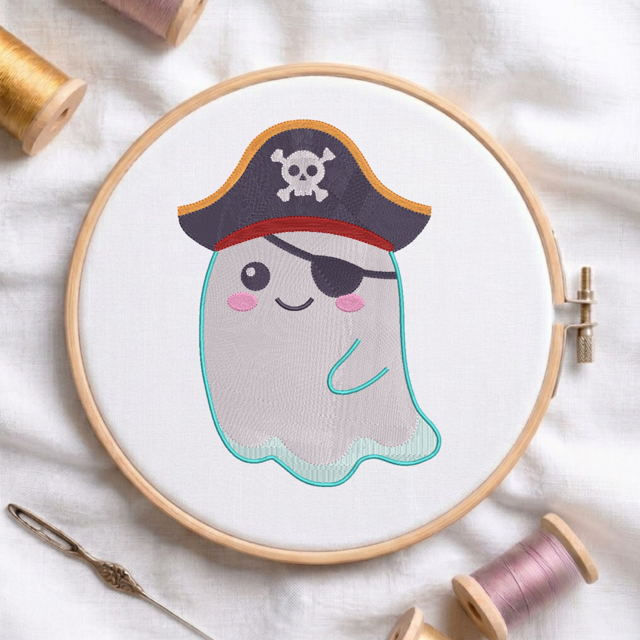 A circular embroidery hoop holds a white fabric with a cartoon ghost design wearing a pirate hat. The hoop is styled on a white fabric background with embroidery thread spools and a needle.