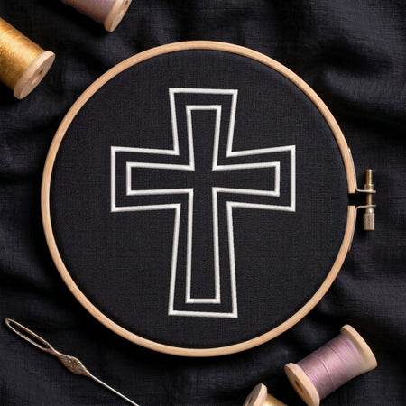 An embroidery hoop on a black cloth displays a finished embroidery design of a clean white outlined Christian cross, flanked by spools of thread and a needle.