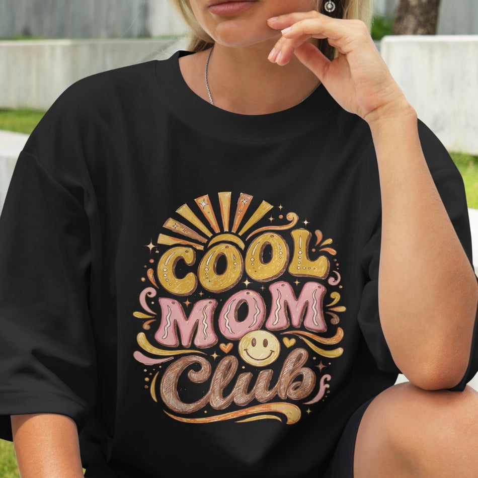 Person wearing a black t-shirt with 'Cool Mom Club' design outdoors.