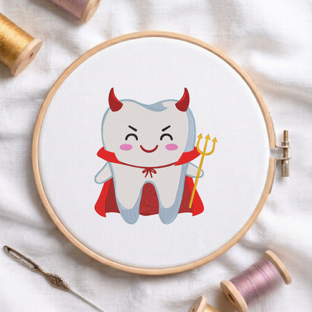 Cute devil tooth wearing horns and a cape while holding a trident machine embroidery design shown in a wooden embroidery hoop on white fabric with thread spools and a needle