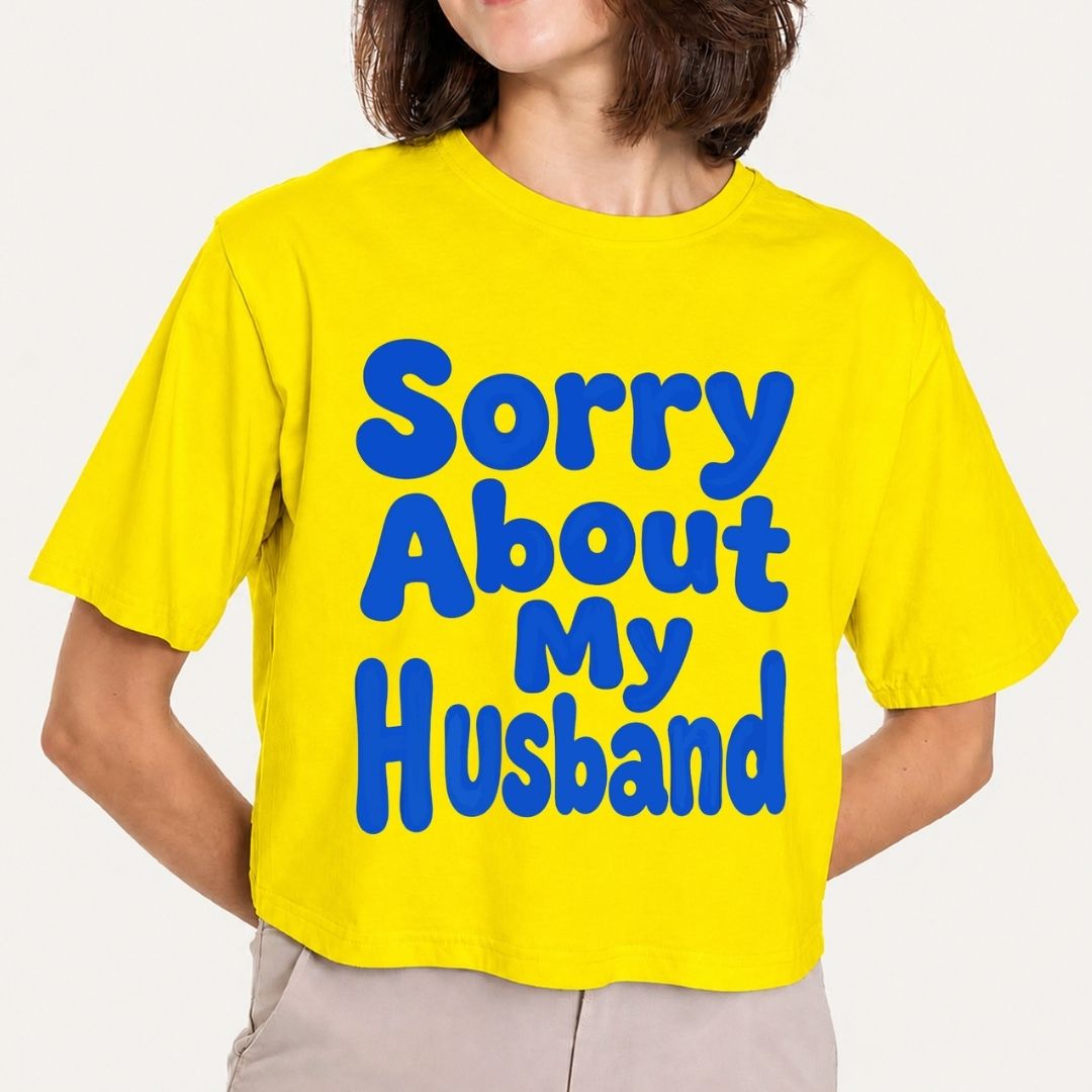 A cropped yellow t-shirt with the phrase 'Sorry About My Husband' printed in large blue bubble letters, worn by a model.