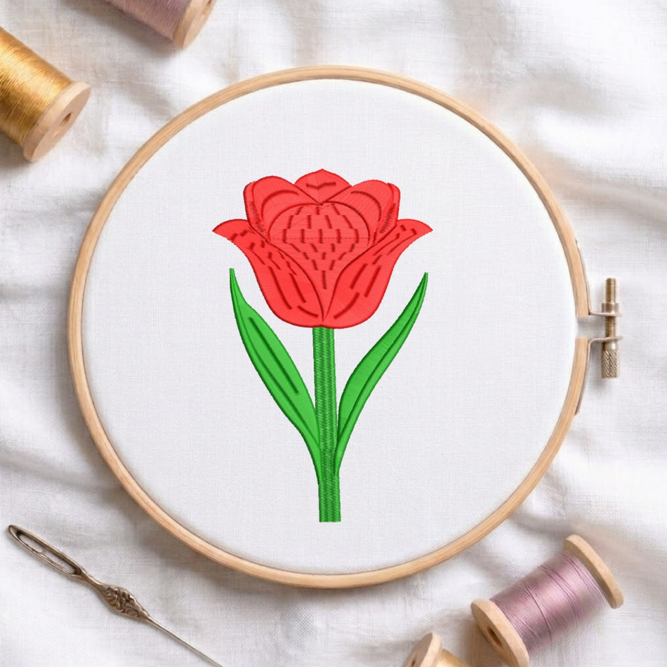 A circular embroidery hoop holding white fabric with a stylized red tulip design outlined in black and filled with red, plus green stems and leaves. The hoop is styled on a white fabric surface with spools of thread and a needle around it.