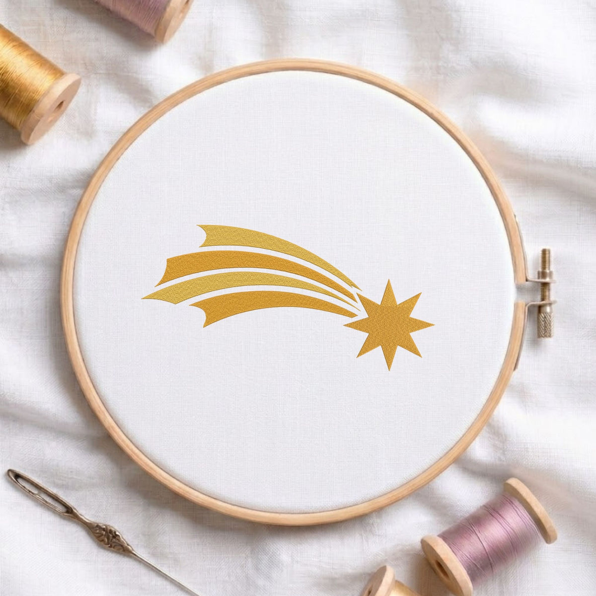  Golden starburst machine embroidery design displayed in a wooden hoop on white fabric with thread spools and a needle   