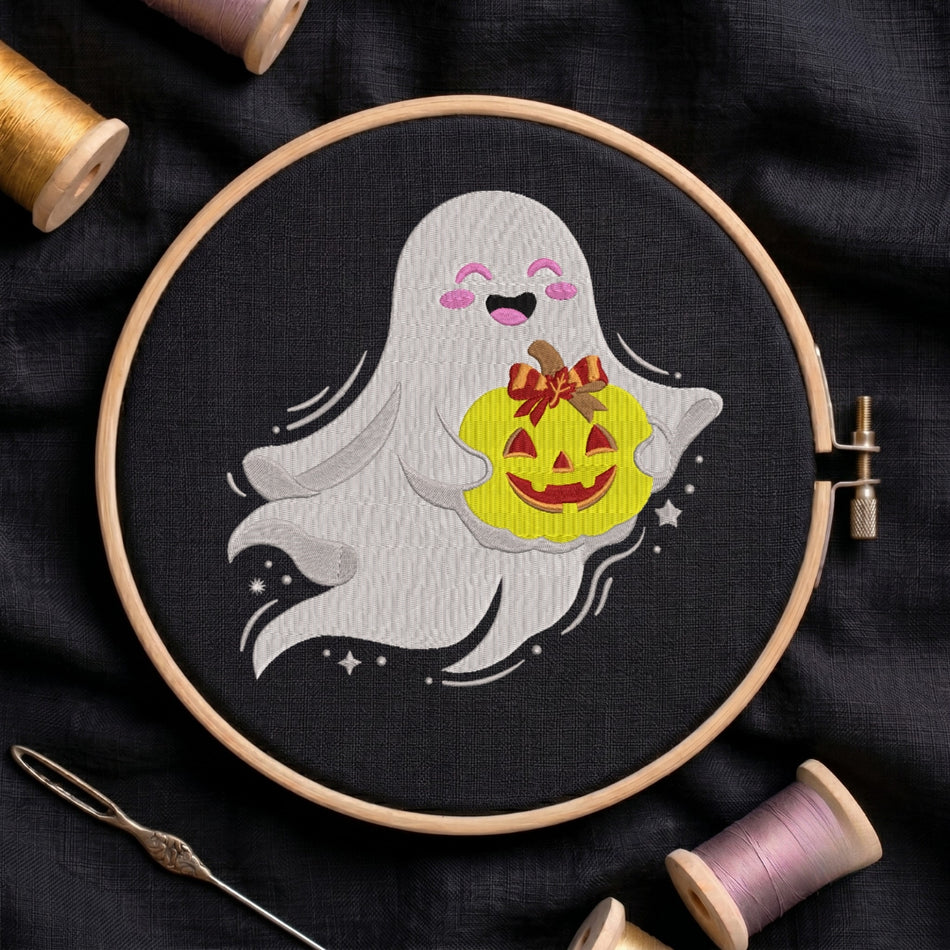The ghost and pumpkin embroidery design centered in a wooden embroidery hoop, positioned on black fabric and surrounded by embroidery thread spools and a needle.