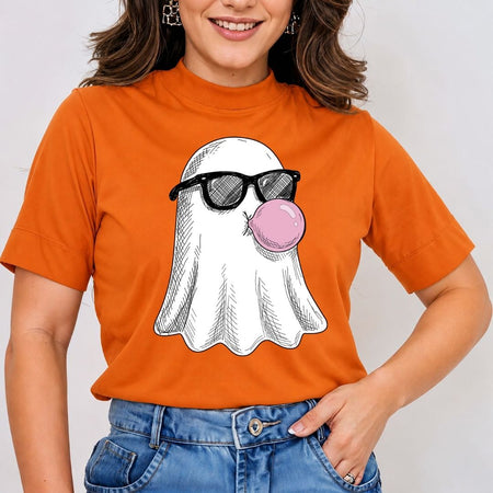 A woman wearing a bright orange short-sleeve t-shirt with a graphic of a white ghost wearing black sunglasses and blowing a pink bubblegum bubble, paired with blue jeans.