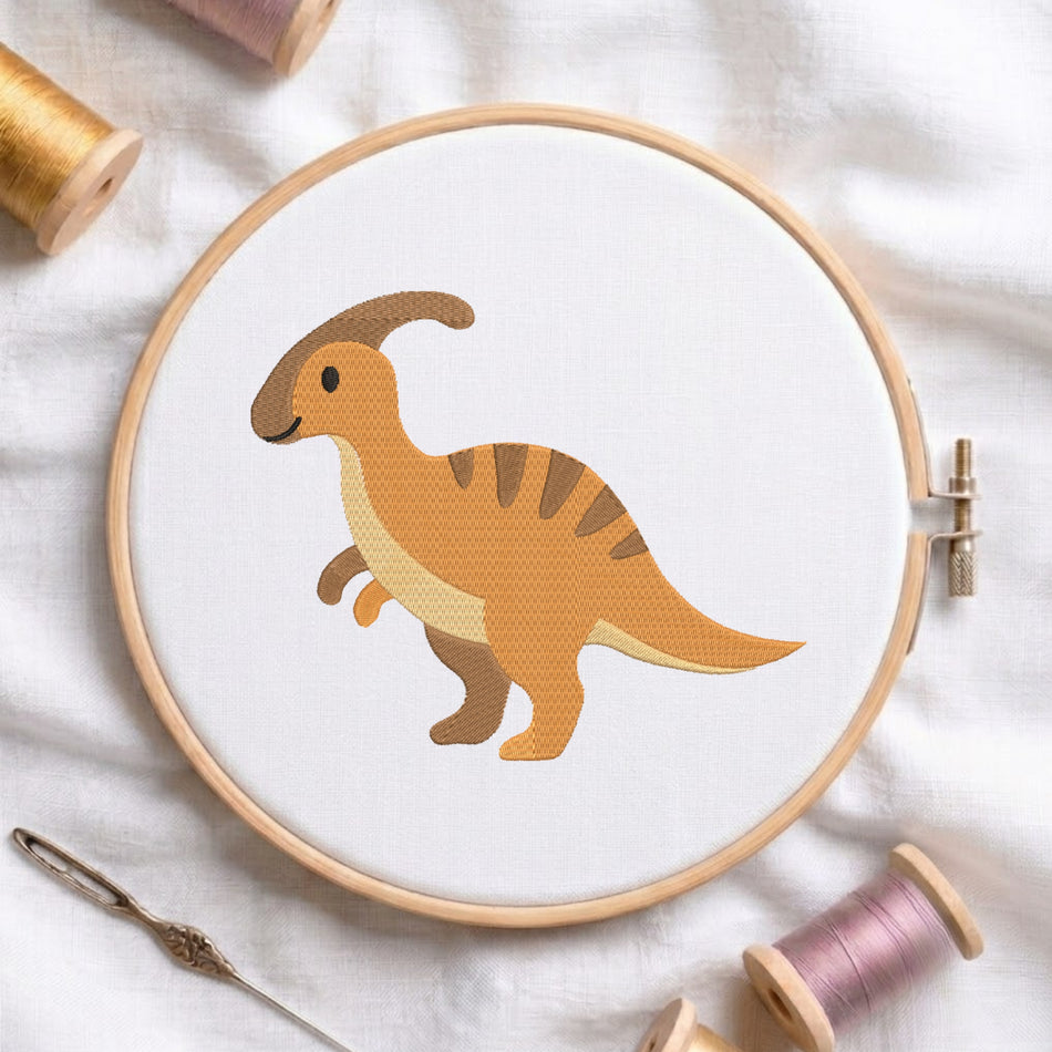 A wooden embroidery hoop holding white fabric with a stylized cartoon dinosaur in tan, brown, and cream stitched onto it. The hoop is styled on a white fabric background with spools of thread and a needle around it.