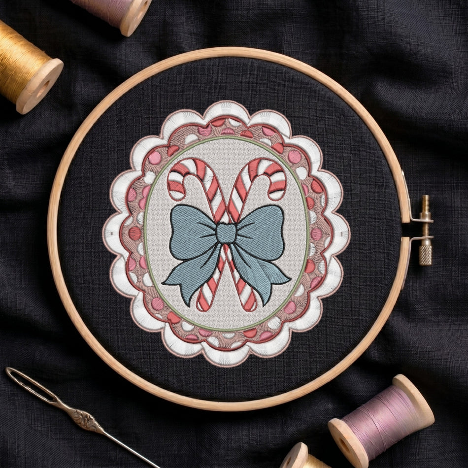 A circular embroidery hoop holding a festive stitched design of two candy canes in a blue bow, surrounded by pink and white scalloped borders, set on dark fabric with spools of thread nearby.