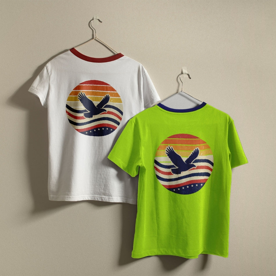 White and lime green t-shirts hanging on a wall, both displaying the vintage sunset and eagle design.