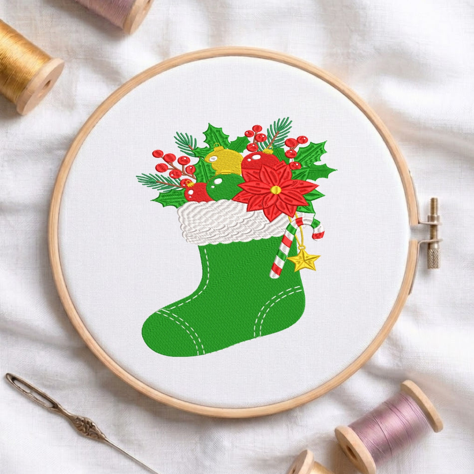 A circular embroidery hoop on white fabric displays a festive Christmas stocking design in green with red poinsettias, holly leaves, candy canes, and gold ornaments. Spools of thread and a needle are arranged around the hoop.